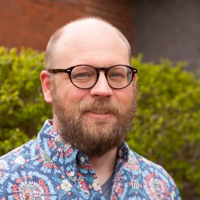 Man wearing dark glasses and colorful, patterned, button up shirt